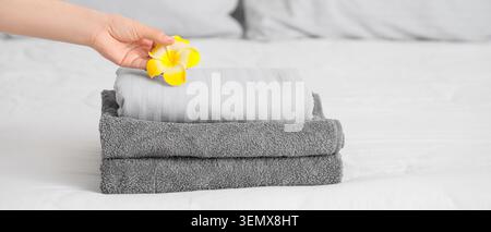 Main plaçant la fleur de plumeria jaune sur la pile de serviettes grises fraîchement pliées et le linge blanc sur le lit Banque D'Images