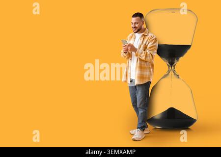 Jeune homme utilisant un smartphone à côté d'un grand sablier, la gestion du temps et le concept d'utilisation des appareils numériques, un jeune homme est activement engagé avec son smartph Banque D'Images