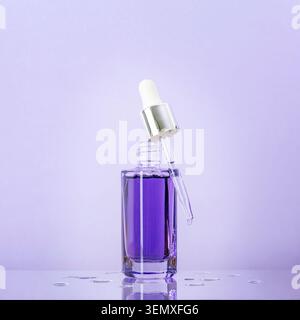 Flacon de sérum violet avec compte-gouttes en verre, liquide cosmétique sur la surface réfléchissante, gouttelettes d'eau. Produit cosmétique pour le soin de la peau Banque D'Images