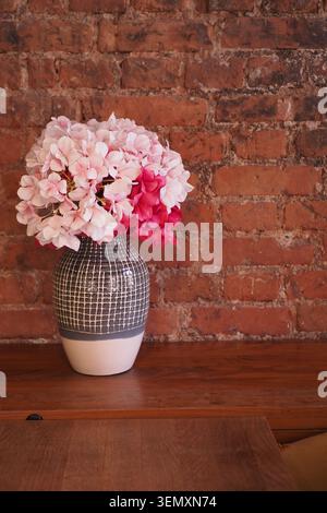 Fleurs dans un vase placé sur une table en bois près du mur de briques Banque D'Images