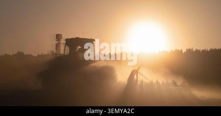 Tracteur effectuant des travaux dans les champs dans un nuage de poussière en plein soleil. Agriculture culture chaleur sécheresse sol sec activité agricole saisonnière et culture Banque D'Images