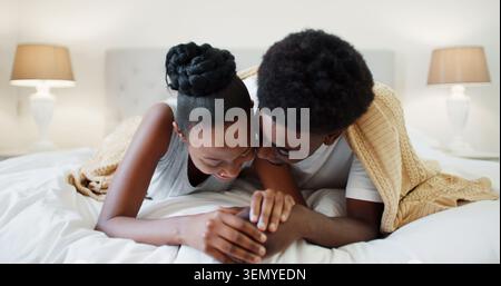 Rire, se détendre et couple noir sur le lit pour la conversation, la connexion et la liaison ensemble dans la maison. Amour, confort et gens heureux avec couverture dans la chambre Banque D'Images