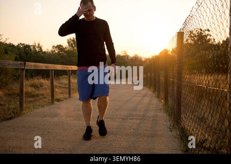 Homme tenant sa tête dans la douleur tout en marchant sur un chemin à l'extérieur au coucher du soleil Banque D'Images