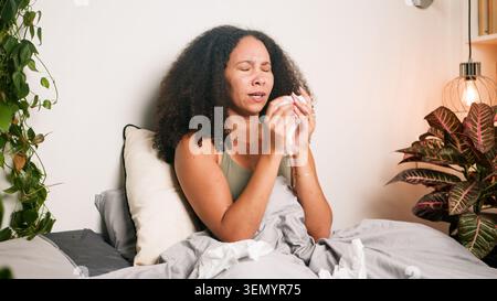 Femme éternuant dans le lit avec des mouchoirs se sentant mal à la maison dans une chambre confortable Banque D'Images