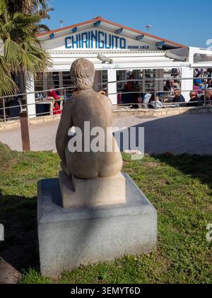Sitges, Espagne - 20 mars 2026 : sculpture en pierre d'une figure assise vue de derrière, surplombant le célèbre bar de plage El Chiringuito sur Sitges Banque D'Images
