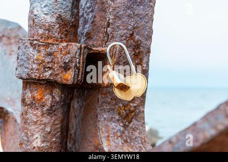 Cadenas Rusty Love avec une étiquette cœur rouge sur une jetée en béton. Vieux cadenas avec un jeton de mariage en forme de coeur attaché à une structure brise-lames. copier spa Banque D'Images