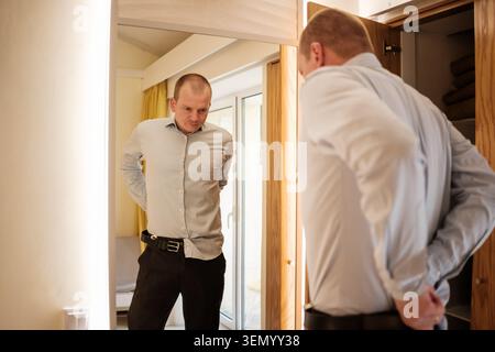Homme s'habillant enfilant sa ceinture et vérifiant son reflet dans un miroir Banque D'Images