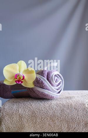 Serviette lilas roulée avec orchidée sur serviette beige sur fond gris avec espace de copie. Banque D'Images