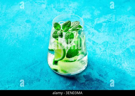 Limonade à la citron vert, ou limeade, dans un verre avec de la citron vert, de la menthe et de la glace. Mojito mocktail ou cocktail d'été frais, sur un fond bleu Banque D'Images