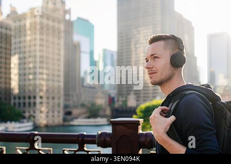 Portrait d'homme mi-adulte avec des écouteurs marchant sur le front de mer dans le centre-ville de Chicago pendant la journée. Style de vie urbain, technologie audio moderne, musique urbaine s Banque D'Images