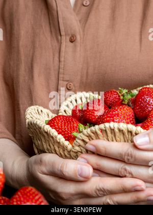 Gros plan de la femme tenant des fraises fraîches mûres dans le panier tissé dans la cuisine. Choix alimentaire sain, récolte saisonnière de fruits, nutrition naturelle et entière Banque D'Images