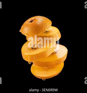 Kiwi doré entier avec des tranches empilées montrant une chair juteuse, isolé sur fond noir avec des gouttelettes de jus visibles. Banque D'Images