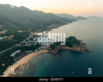 Vue aérienne du village côtier niché entre montagnes et rivage serein au coucher du soleil. Banque D'Images