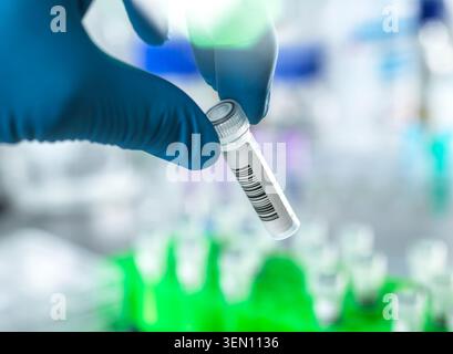 Main gantée tenant un tube à essai avec code-barres dans un environnement de laboratoire. Banque D'Images