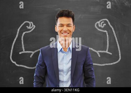 Homme asiatique représenté comme un homme d'affaires prospère debout devant une planche avec des dessins de bras musclés Banque D'Images