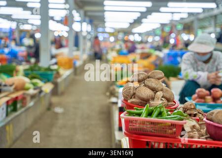 Champignons shiitake frais concentrés au premier plan sur le marché traditionnel de cinq jours de Jeju, avec un vendeur de personnes âgées floues en arrière-plan. Banque D'Images