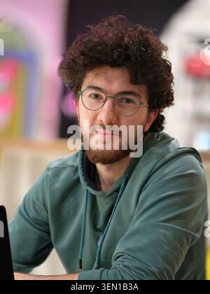 Jeune homme portant des lunettes et un sweat à capuche vert assis à l'intérieur, portrait décontracté avec expression réfléchie Banque D'Images