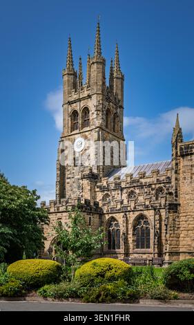 Vue portrait vertical mettant en évidence l'imposante tour de pierre de style perpendiculaire et les façades extérieures de l'église Saint-Jean-Baptiste à Tideswell, Derby Banque D'Images