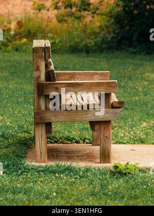 Un banc vide en bois rustique altéré reposant sur une dalle de béton entourée d'herbe verte luxuriante et d'un champ de trèfles Banque D'Images
