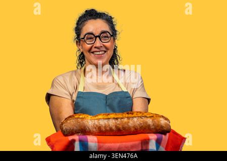 Femme mature boulanger portant un tablier et tenant fièrement un pain frais Banque D'Images
