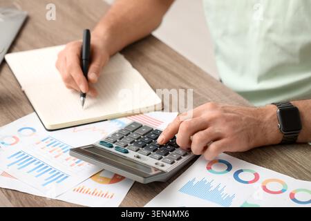 Mains masculines écrivant quelque chose et faisant des calculs au bureau. Gros plan Banque D'Images