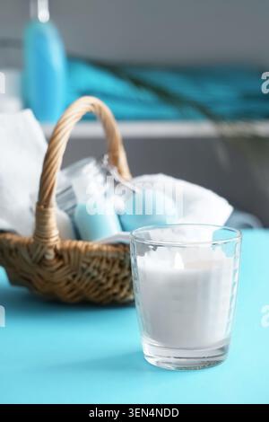 Essentiels de la journée de spa relaxant avec bougie allumée et panier en osier de produits de bain sur fond bleu, une bougie blanche allumée dans un support en verre se trouve sur une vibr Banque D'Images