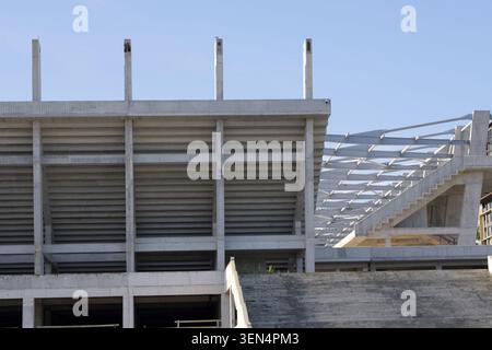 Nouveau processus de construction du stade avec des tribunes en béton armé, des piliers et des composants en acier pour le toit et les escaliers extérieurs sur un bleu clair Banque D'Images