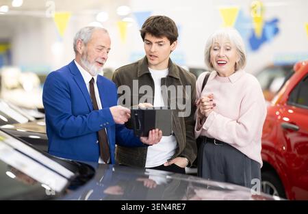 La fille adulte aide sa mère âgée à choisir une nouvelle voiture chez un concessionnaire automobile. Banque D'Images