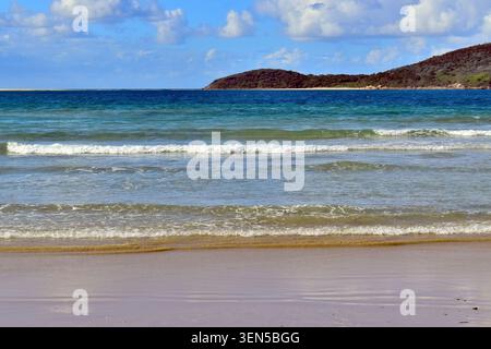 Les vagues douces se jettent sur une plage de sable pâle, passant du bleu clair au turquoise profond lorsqu'elles rencontrent l'eau libre. Banque D'Images