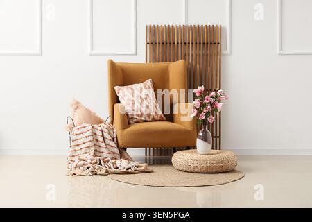 Intérieur confortable du salon avec fauteuil moutarde, oreillers décoratifs, tapis tissé et fleurs roses dans le vase Banque D'Images