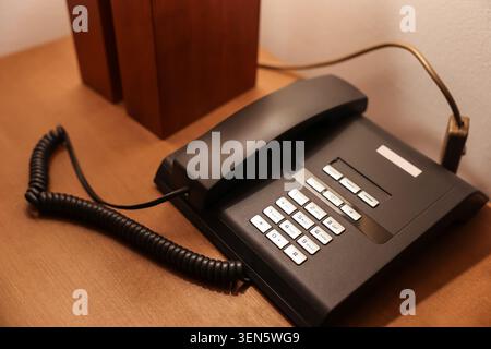 Téléphone de bureau noir avec boutons blancs et cordon enroulé sur la table en bois, technologie de communication, cette technologie de communication représente les affaires et c Banque D'Images