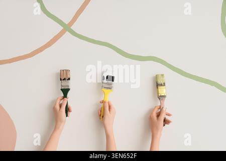 Trois mains tenant des pinceaux de différentes couleurs, la rénovation créative de la maison et le concept de design d'intérieur, les pinceaux sont positionnés contre un wh Banque D'Images