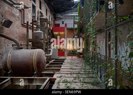 L'intérieur restauré de l'Arche Hotel Cukrownia comprend un grand réservoir en métal rouillé, des murs en briques apparentes, des plantes vertes et un escalier rouge moderne Banque D'Images