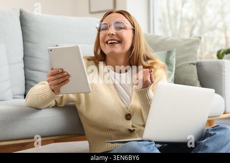 Femme heureuse utilisant tablette numérique et ordinateur portable à la maison, travail à distance et succès d'apprentissage en ligne, style de vie technologique moderne Banque D'Images