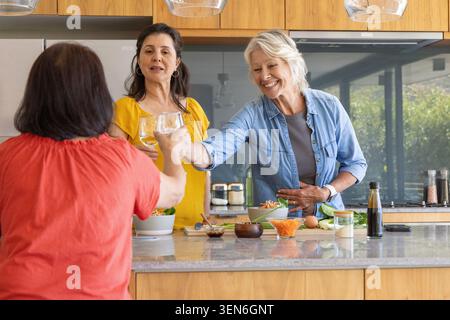 Diverses amies féminines, femmes âgées et matures, cuisiner et griller avec du vin dans la cuisine Banque D'Images