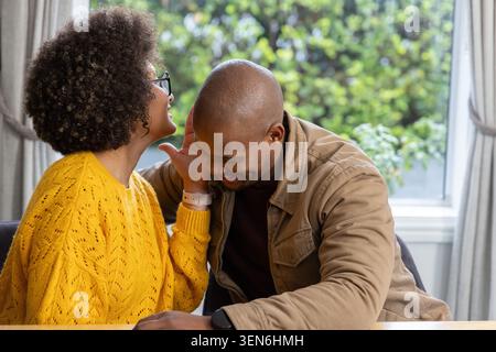Couple par table assise de fenêtre, femme en tricot jaune touchant African American Man tan veste Watch Banque D'Images
