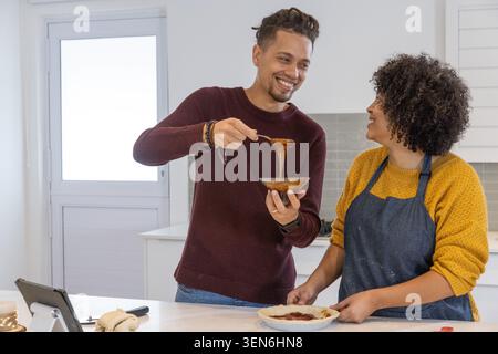 Couple, femme dans le tablier et homme dans le pull en tricot, préparant la tarte à l'îlot de cuisine avec bol Banque D'Images