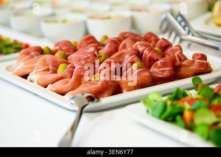 Un plat de buffet magnifiquement arrangé avec des plis élégants de prosciutto haut de gamme associés à des olives vertes éclatantes. Le gros plan met en évidence le Banque D'Images
