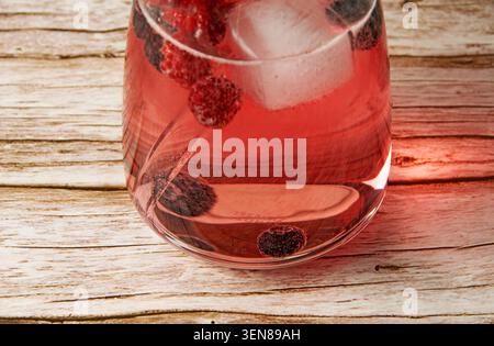 Gros plan d'une boisson rafraîchissante aux baies avec des baies congelées et des glaçons dans un verre sur un fond en bois rustique. Banque D'Images