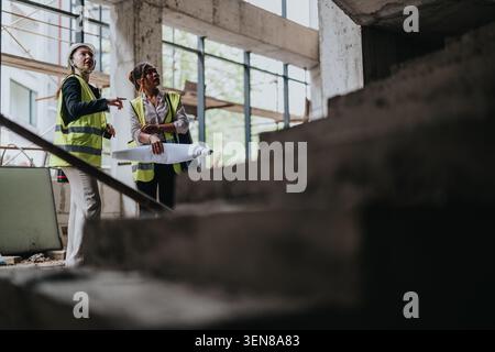 Deux femmes ingénieurs inspectant un chantier avec des plans et des gilets haute visibilité Banque D'Images
