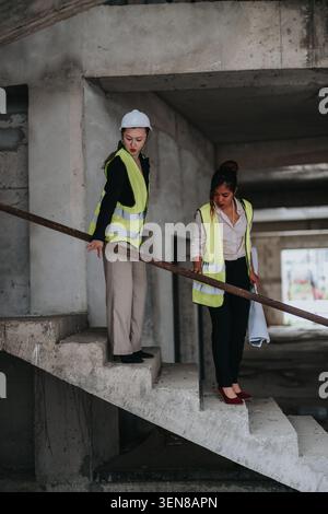 Deux femmes ingénieurs inspectant une cage d'escalier de chantier inachevée en gilets de sécurité et casque de sécurité Banque D'Images