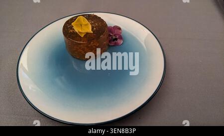Gros plan d'un dessert de classe affaires exquis : gâteau au chocolat avec accent de feuilles d'or, servi sur une assiette bleue moderne dégradé Banque D'Images