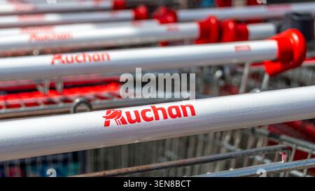 Pancartes sur les poignées des chariots à l'extérieur d'un magasin Auchan en France. Auchan est une multinationale française de distribution qui possède de nombreux supermarchés Banque D'Images