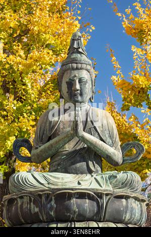 Statue de Bouddha en pierre assise en méditation entourée de feuilles de ginkgo jaune doré d'automne, Tokyo, Japon Banque D'Images