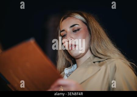 Jeune femme d'affaires lisant un menu ou un document la nuit portant un trench-coat et le maquillage Banque D'Images