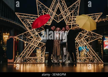 Amis et collègues d'affaires célébrant sous les lumières de Noël avec des parapluies dans la nuit de la ville Banque D'Images