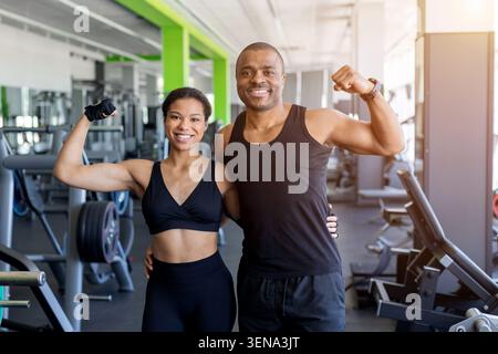 Jeune noir posant en toute confiance dans la salle de gym moderne, fléchissant les muscles après l'entraînement Banque D'Images