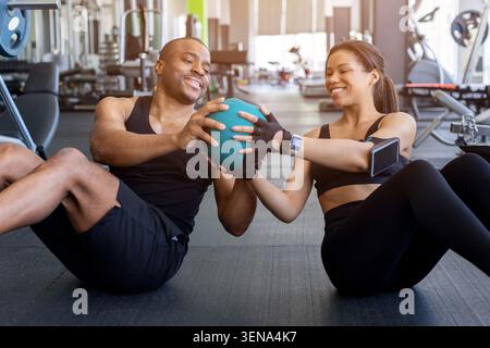 Jeune fitness noir effectuant des exercices de noyau de medecine ball ensemble dans le gymnase Banque D'Images