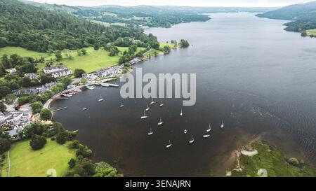 Un vaste lac est parsemé de nombreux voiliers, avec un charmant village niché le long de sa rive bordée d'arbres et des collines verdoyantes dans l'arrière-pays Banque D'Images