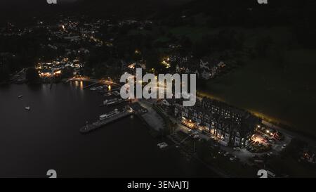 Une perspective aérienne capture un village côtier tranquille illuminé par des lumières chaudes contre le ciel nocturne sombre, mettant en valeur un port serein et surrou Banque D'Images
